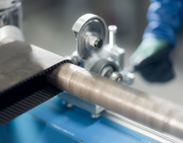 Close-up of a moving roller mechanism with striped material running through it in an industrial setting.