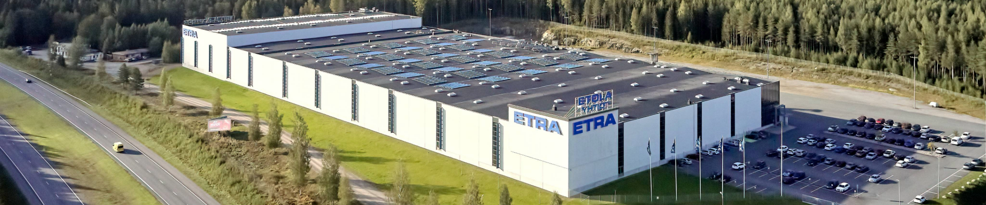 Exterior view of Etra's logistics center – a large, modern warehouse building with the company logo prominently displayed. In the background, an open sky and a spacious yard area.