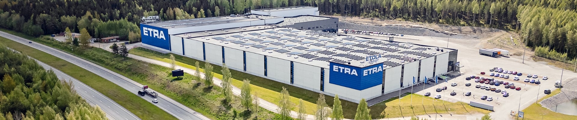 Exterior view of Etra's logistics center &ndash; a large, modern warehouse building with the company logo prominently displayed. In the background, an open sky and a spacious yard area.