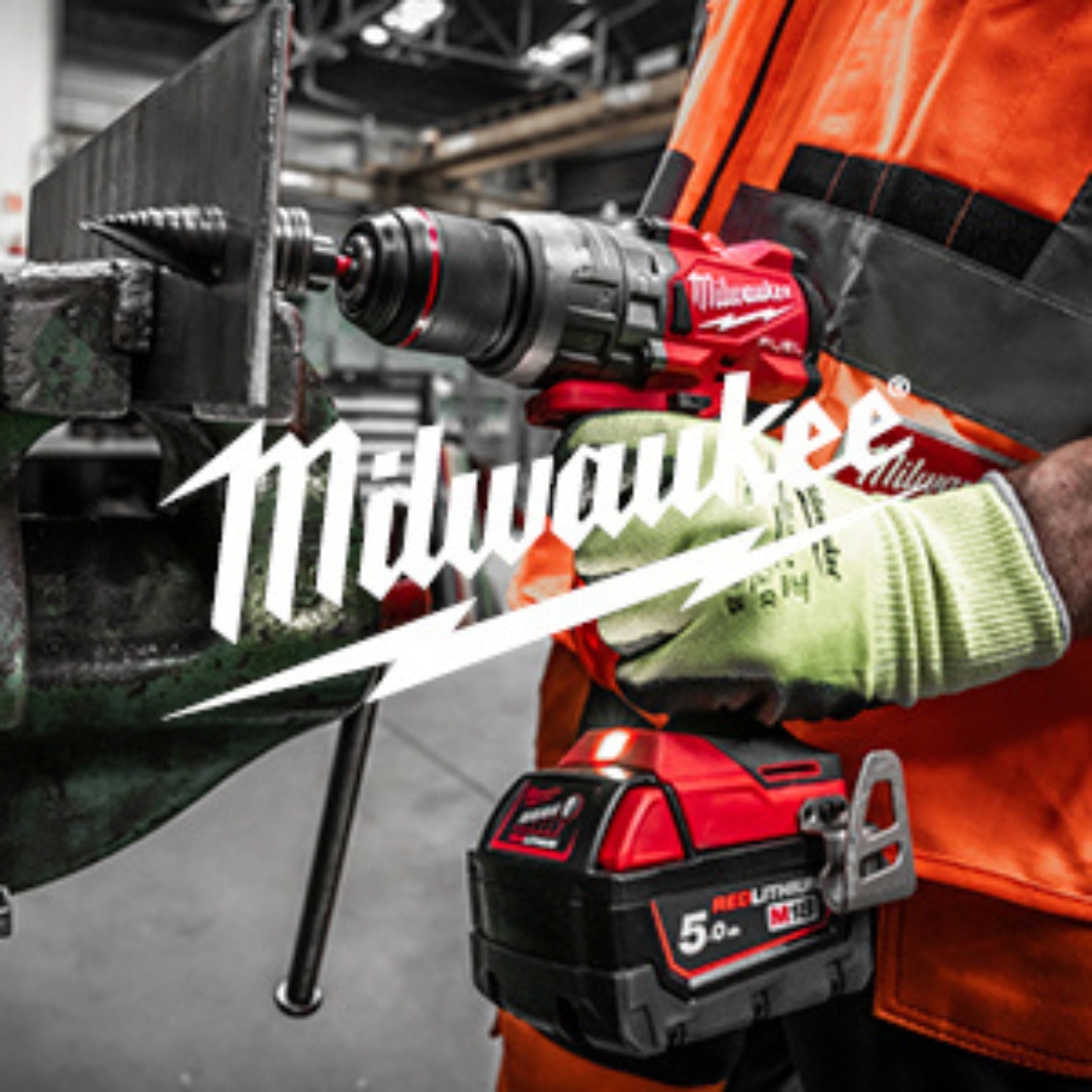 Työntekijä käyttää Milwaukee-merkkistä akkukäyttöistä porakonetta teollisuusympäristössä. Porakone on punamusta ja siinä on näkyvissä REDLITHIUM-akku. Henkilö käyttää turvaliivejä ja suojakäsineitä