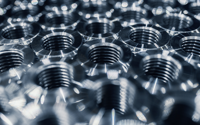 Close-up of shiny metallic nuts with threaded interiors. The smooth and polished surfaces of the nuts reflect light.