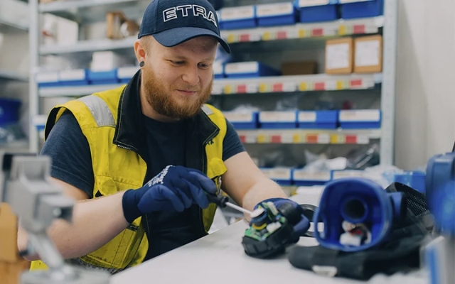 Etra employee repairing or assembling parts of a respirator at a workstation, with storage shelves in the background.