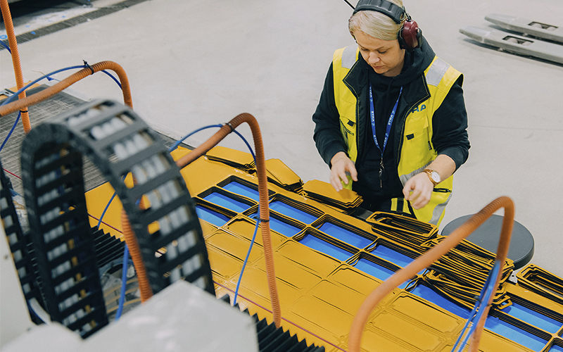 A person wearing a yellow safety vest and headphones is working with rubber material. A forklift is visible in the background.
