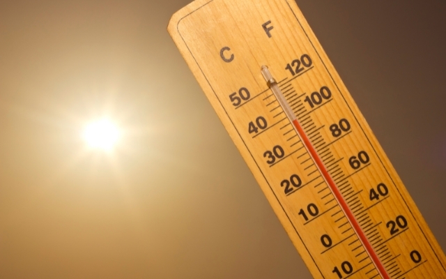 Puinen lämpömittari, joka näyttää korkeaa lämpötilaa auringon paistaessa kirkkaasti taustalla. Mittari näyttää yli 40 °C:n lämpötilaa, viitaten erittäin kuumaan säähän.