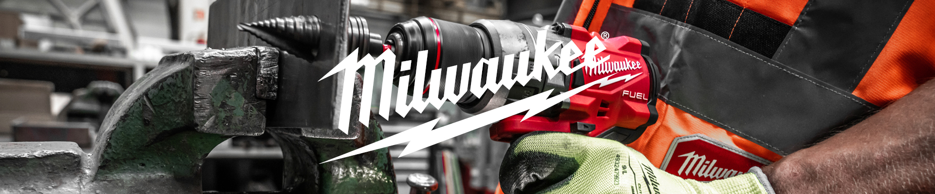 "Työntekijä käyttää Milwaukee-merkkistä akkukäyttöistä porakonetta teollisuusympäristössä. Porakone on punamusta ja siinä on näkyvissä REDLITHIUM-akku. Henkilö käyttää turvaliivejä ja suojakäsineitä."