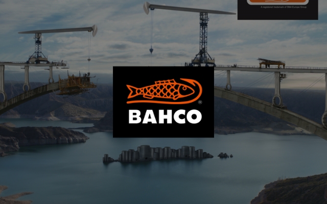 Rakenteilla oleva silta korkealla vuoristomaisemassa, jossa on rakennusnostureita ja työkoneita. Kuvan keskellä on musta Bahco-logo.