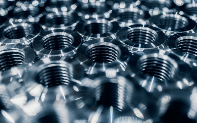 Close-up of shiny metallic nuts with threaded interiors. The smooth and polished surfaces of the nuts reflect light.