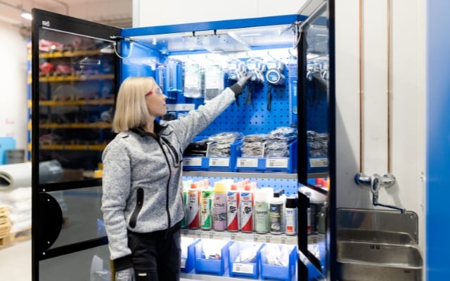 En kund undersöker ett verktygsskåp i ETRA:s serviceförråd, innehållande blå lådor, verktyg och smörjmedel. Skåpet är väl upplyst och i bakgrunden syns lagringshyllor.