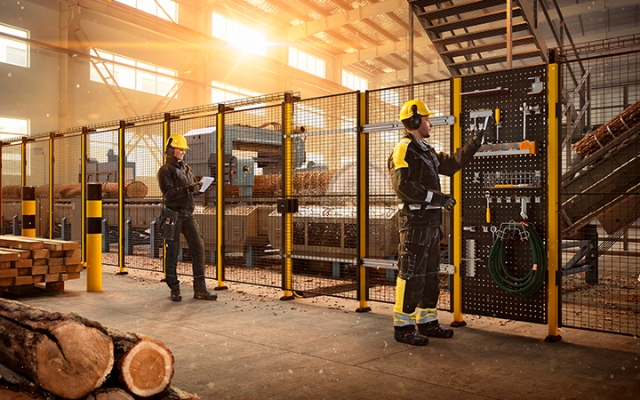 Wood industry production area where workers wear protective gear and operate machines within the safety fencing.