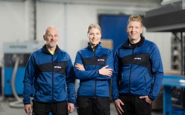 Three Etra employees in blue workwear in an industrial environment.