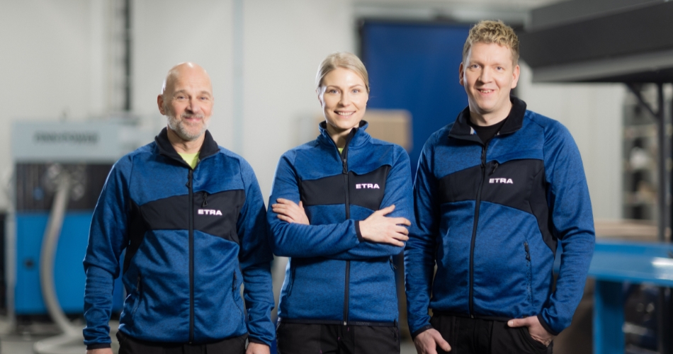 Three Etra employees in blue workwear in an industrial environment.